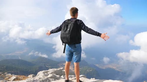 Hiker with Backpack Standing on Mountain Edge and Raising His Hands Enjoying Freedom. Man Actively