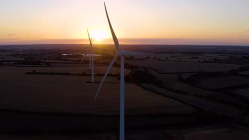 Große Windturbinen mit Rotorblättern im Feld, Luftbild, leuchtend orangefarbener Sonnenuntergang.