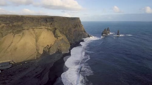 Aerial view of black beach with big waves and cliffs in Vik, Iceland