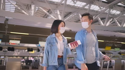 Man and woman couple passengers wearing face mask walking in airport terminal to boarding gate.