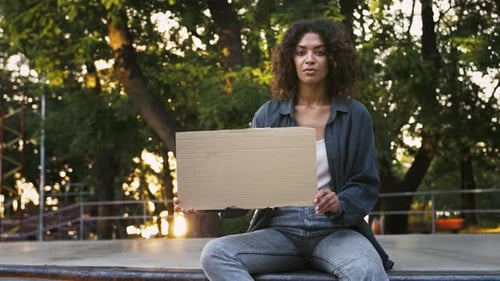 Afroamerican Female Holding Empty Cardboard Tablet Sitting on Pump Track at Sunny Skatepark