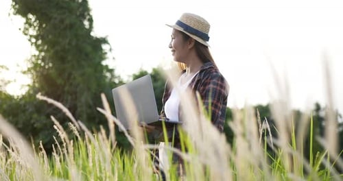 Farmer woman holding laptop and smiling in field