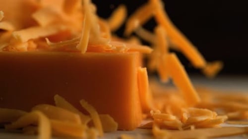 Kamera folgt dem Reiben von Cheddar-Käse. Zeitlupe.