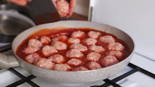 Raw Meatballs Simmering in Red Sauce on Stove