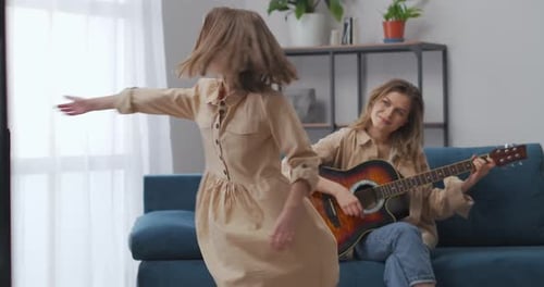 Woman Plays Guitar as Girl Dances at Home