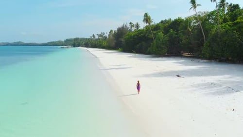 Aerial Slow motion: woman walking on white sand beach turquoise water tropical coastline