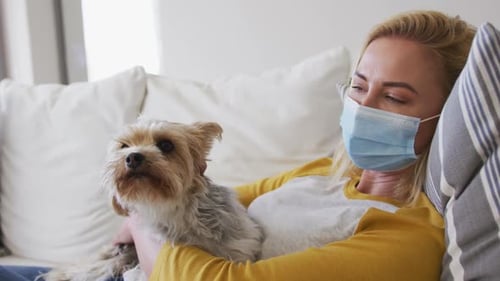 Woman wearing face mask holding her pet dog at home