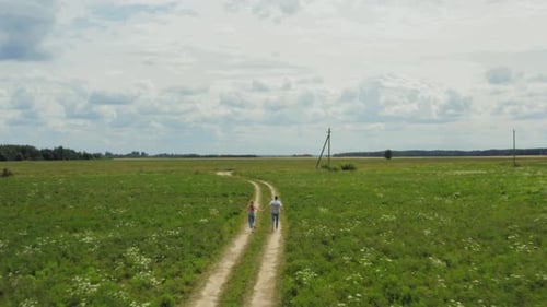 Aerial View Of Playful Couple Holding Hands And Running Rural Road. Camera Is Ahead of Them. Shot.