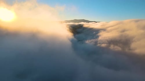 Luftaufnahme der Landschaft über nebligen, sich schnell bewegenden Wolken, die die Berghügel bei Sonnenuntergang bedecken.