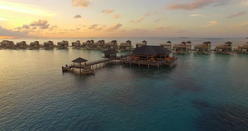 Aerial drone view sunset scenic tropical island, resort hotel with overwater bungalows, Maldives.