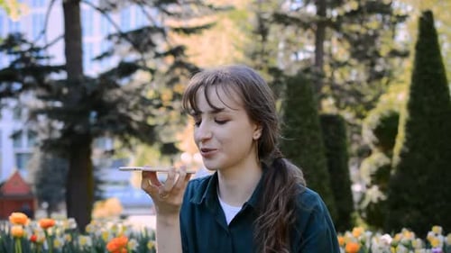 Beautiful Young Caucasian Girl Talking on the Phone in a City Park in Summer