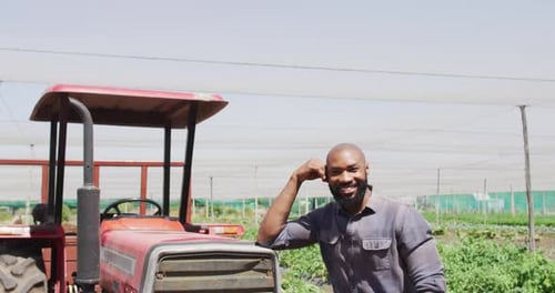 Smiling Farmer Leans on Tractor near Crops
