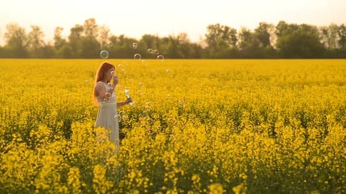 Young Redhair Woman Blowing Bubbles at the Camera Outdoors in Summer Meadow
