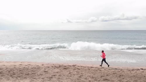 Woman Jogging on Sandy Beach by Ocean