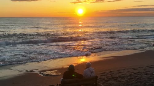 People sit on the beach and watch the sunset