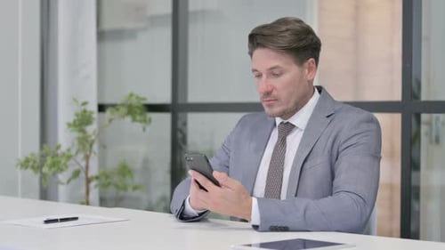 Attractive Middle Aged Man using Smartphone in Office