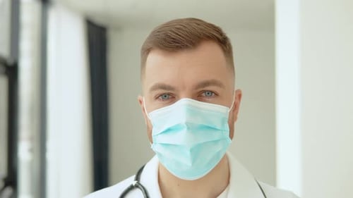 Successful Physician in White Lab Coat and Mask Looks at the Camera and Smiles in Hospital Office