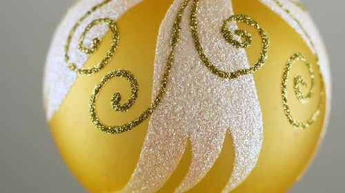 Golden Christmas ball toy turning round and back in luminous light on dark green background.