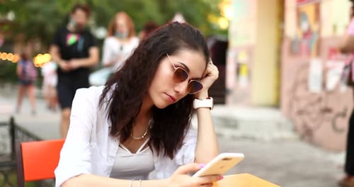 Woman Uses Phone at Outdoor Cafe Table
