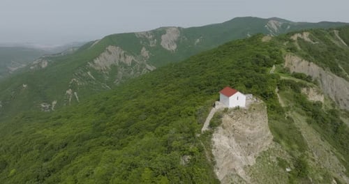 Vue aérienne en grand angle d'un petit bâtiment entouré de collines boisées.