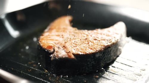 A Salmon Fillets on a Grill Plate is Sprinkling Spices