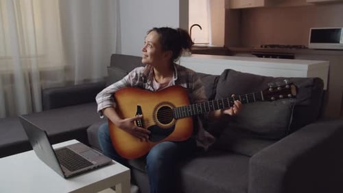 Woman Plays Guitar on Couch in Home
