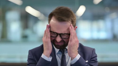Man with Headache Rubbing Temples in Office