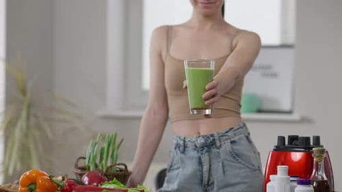 Slim Young Unrecognizable Caucasian Woman Stretching Glass of Healthful Green Smoothie Smiling