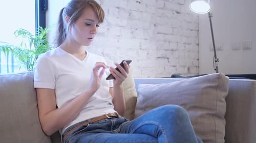 Young Woman Uses Smartphone on Couch, Shows Surprise