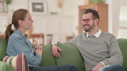 Feliz pareja conversando mientras está sentada en el sofá