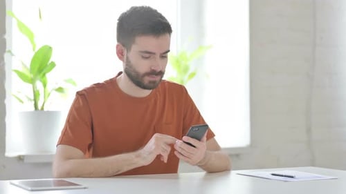 Man Using Smartphone at Desk Receives Good News
