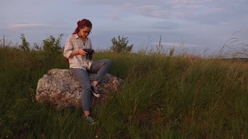 Woman Photographer Sitting on Rock in Grassy Field