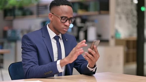 African Businessman Celebrating Success on Smartphone in Office