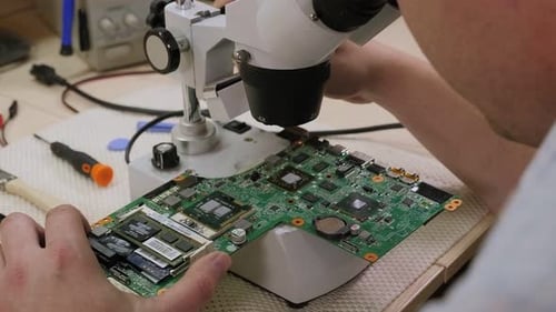 Repairman Repairing Computer in Service Center with the Help of a Microscope.
