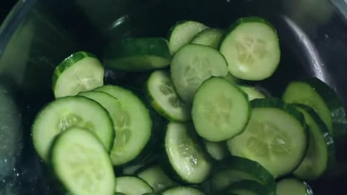 Sliced Cucumbers Dropping into Stainless Steel Bowl