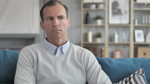 Nachdenklicher Mann mittleren Alters sitzt auf der Couch im kreativen Büro
