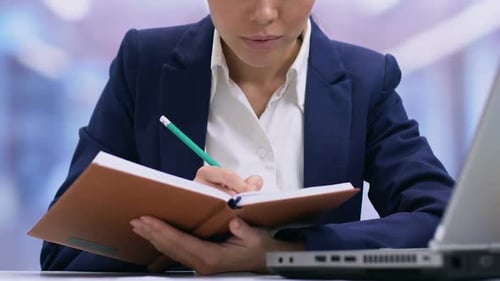 Woman Writing in Notebook at Desk with Laptop