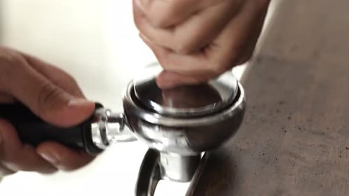 Hands tamping espresso with metal tamper