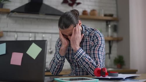 Man Working at Laptop Massaging Temples in Kitchen