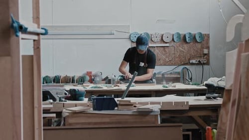 Man in a Carpentry Workshop Grinding a Wooden Piece