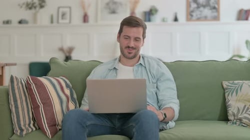 Young Adult Video Calling on Laptop from Couch