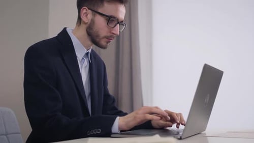 Side View Portrait of Handsome Caucasian Businessman in Eyeglasses Typing on Laptop. Young