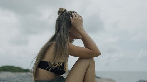 Young Woman Sitting sadly on a Rocky Beach