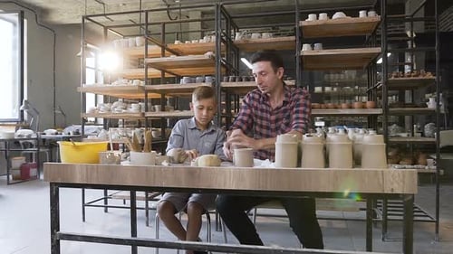 Boy and Man Shaping Clay Together in Workshop