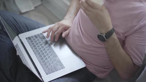 Ein unbekannter Mann sitzt am Fenster und tippt auf einem Laptop, während er Kaffee trinkt