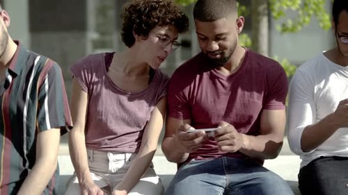Front View of Two Friends Sitting and Looking at Smartphone