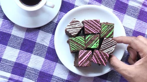 Hand Takes Decorated Brownie from Plate with Coffee