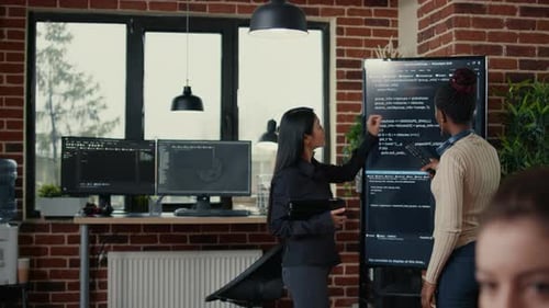 Software Engineers Analyzing Code on Wall Screen Tv Looking for Bugs and Errors While Colleague