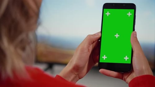 Woman at Home Sitting on a Couch using Smartphone with Green Mock-up Screen