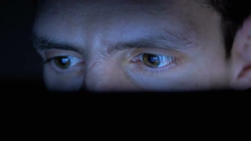 Mann im Hut schaut nachts auf einen Laptop-Monitor